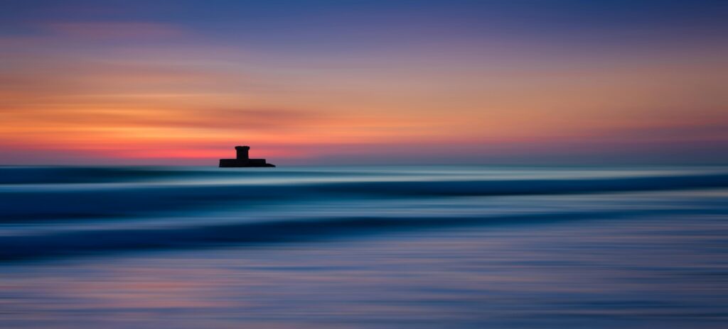 A tranquil view of St. Ouen's Bay with a colorful sunset on the horizon.